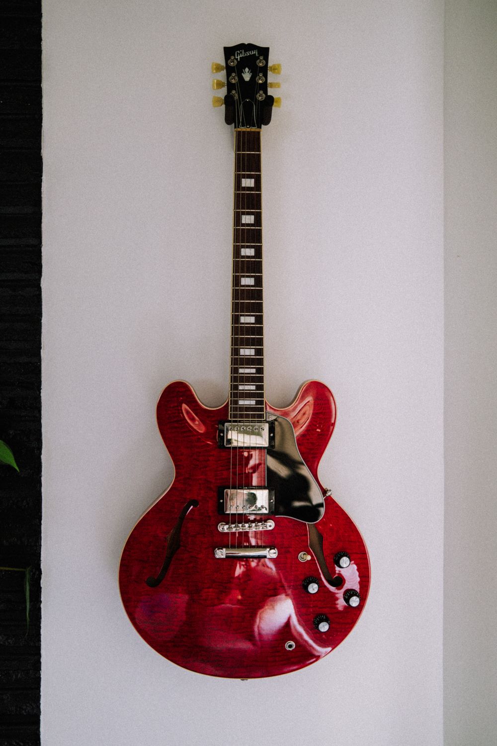 A cherry red semi-hollow electric guitar hanging on a white wall