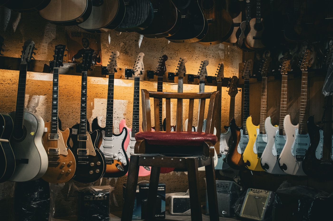 A guitar shop at night, rows of electric and acoustic guitars on the walls and a stool in the middle