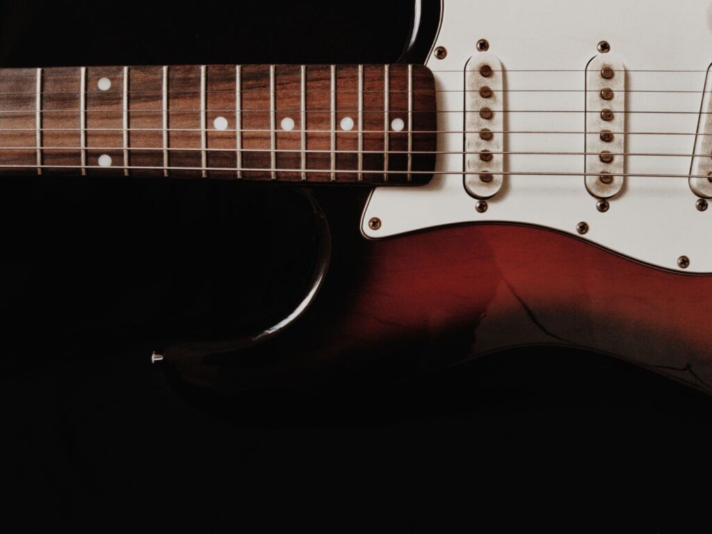 Close-up of the strings, pickups and red body of an electric guitar against a dark background