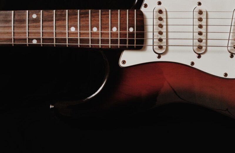 Close-up of the strings, pickups and red body of an electric guitar against a dark background