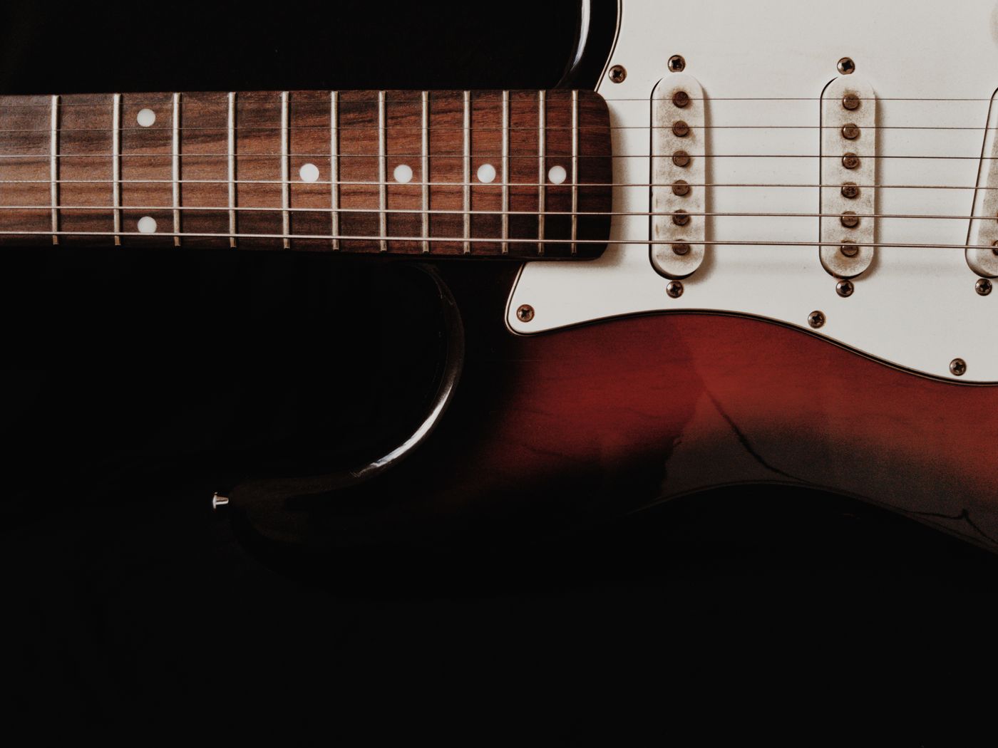 Close-up of the strings, pickups and red body of an electric guitar against a dark background