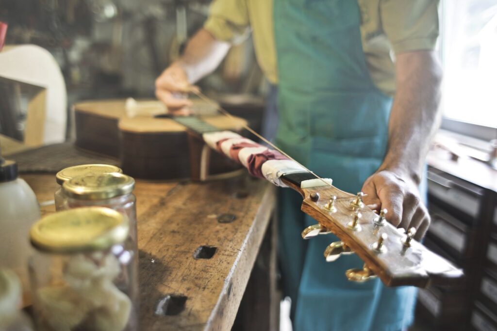 A luthier's hands fitting tuners to a guitar headstock on a wooden workbench