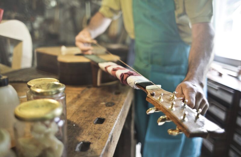 A luthier's hands fitting tuners to a guitar headstock on a wooden workbench