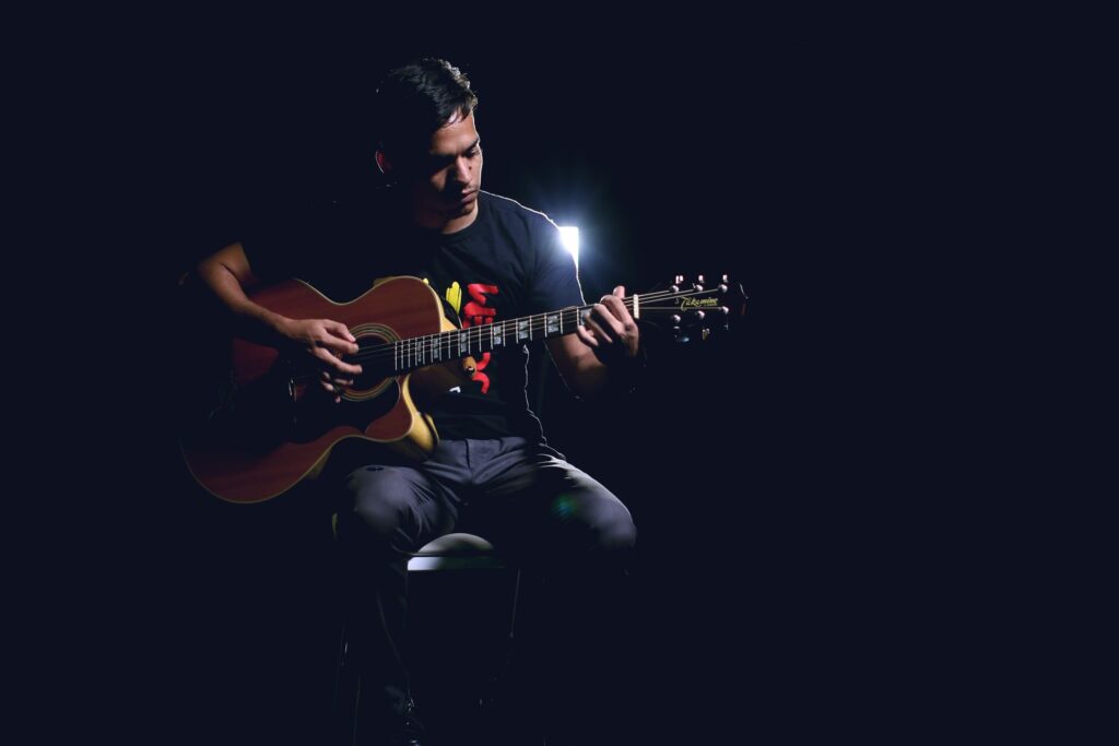 A guitarist playing an acoustic guitar on a dim stage under a single light