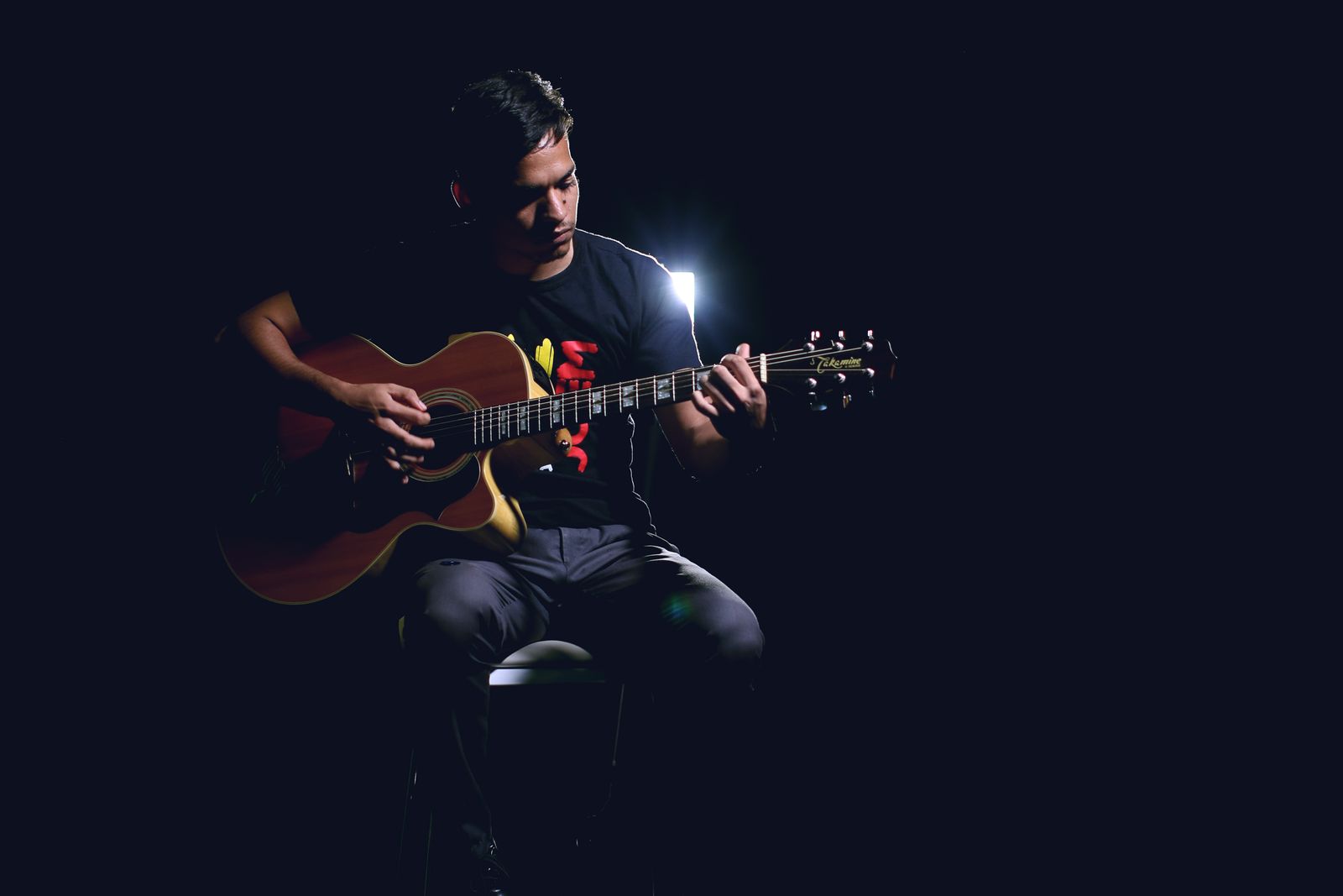 A guitarist playing an acoustic guitar on a dim stage under a single light