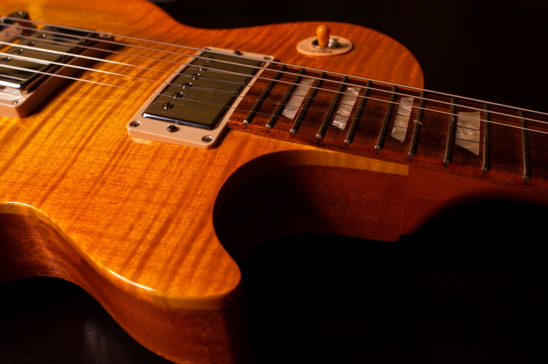The flame maple top and humbucker pickups of an amber electric guitar on a black background