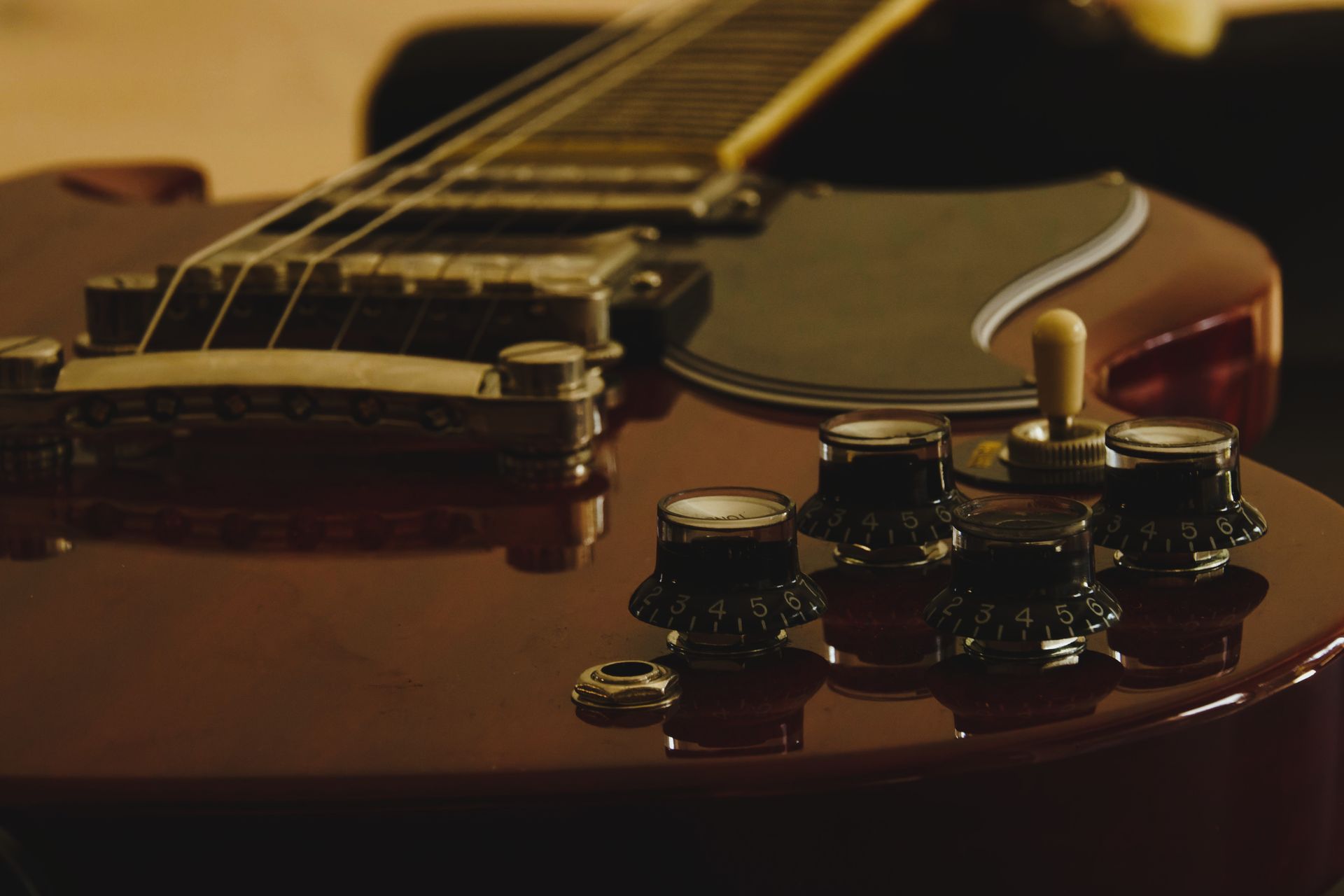 Control knobs, pickups and bridge of a sunburst electric guitar in warm low light