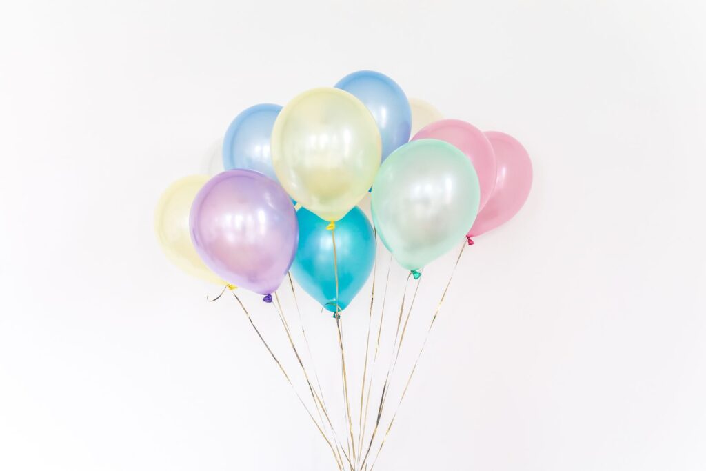 A bunch of pastel balloons on long ribbons against a white wall