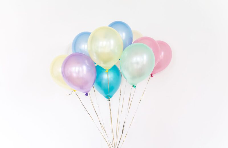 A bunch of pastel balloons on long ribbons against a white wall