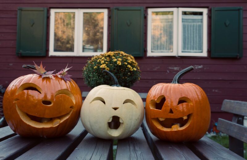 Three carved pumpkins with funny faces on a wooden table outdoors