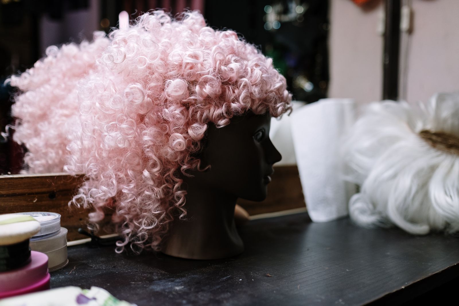 A curly pink wig on a mannequin head in a dressing room
