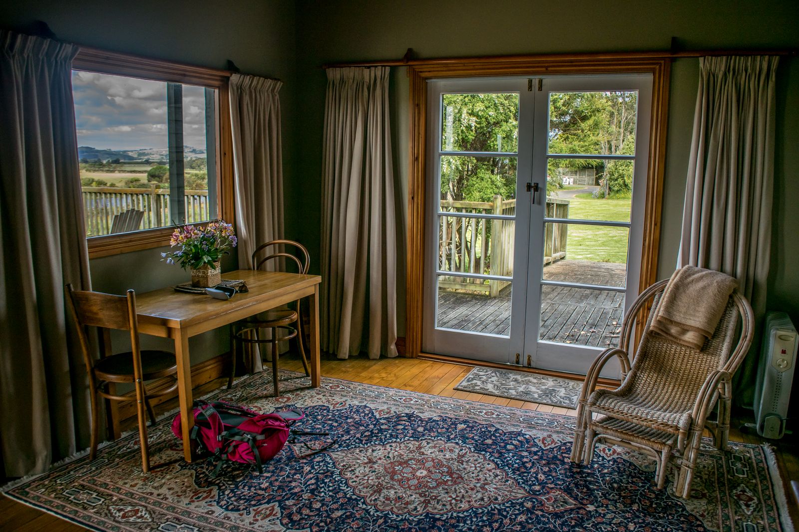 A room with a writing desk, a rug and glass doors open onto a green garden