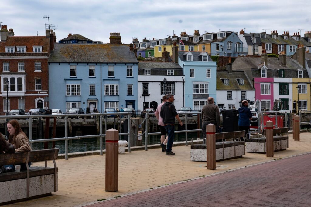 Painted houses along a harbour front, people walking by the water in the distance