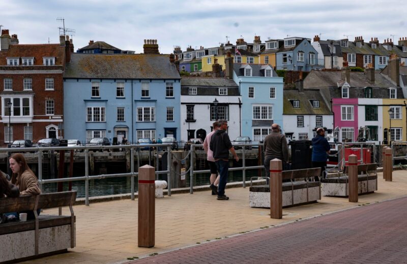 Painted houses along a harbour front, people walking by the water in the distance