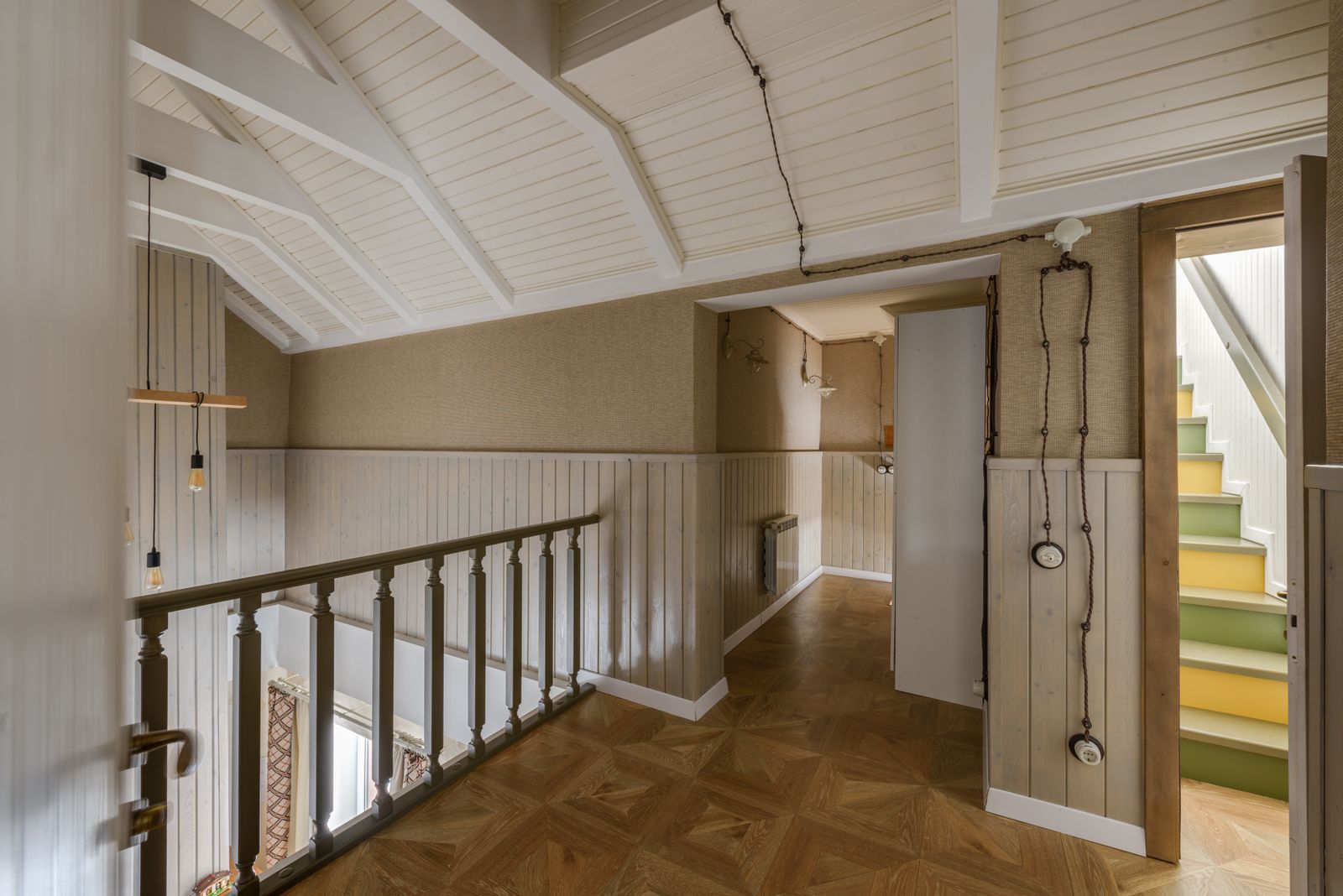 An upstairs landing with a wooden floor, a white railing and painted stairs going up to the attic