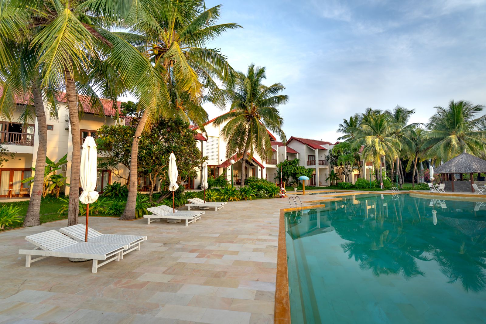 An outdoor pool with sun loungers and palm trees beside the hotel