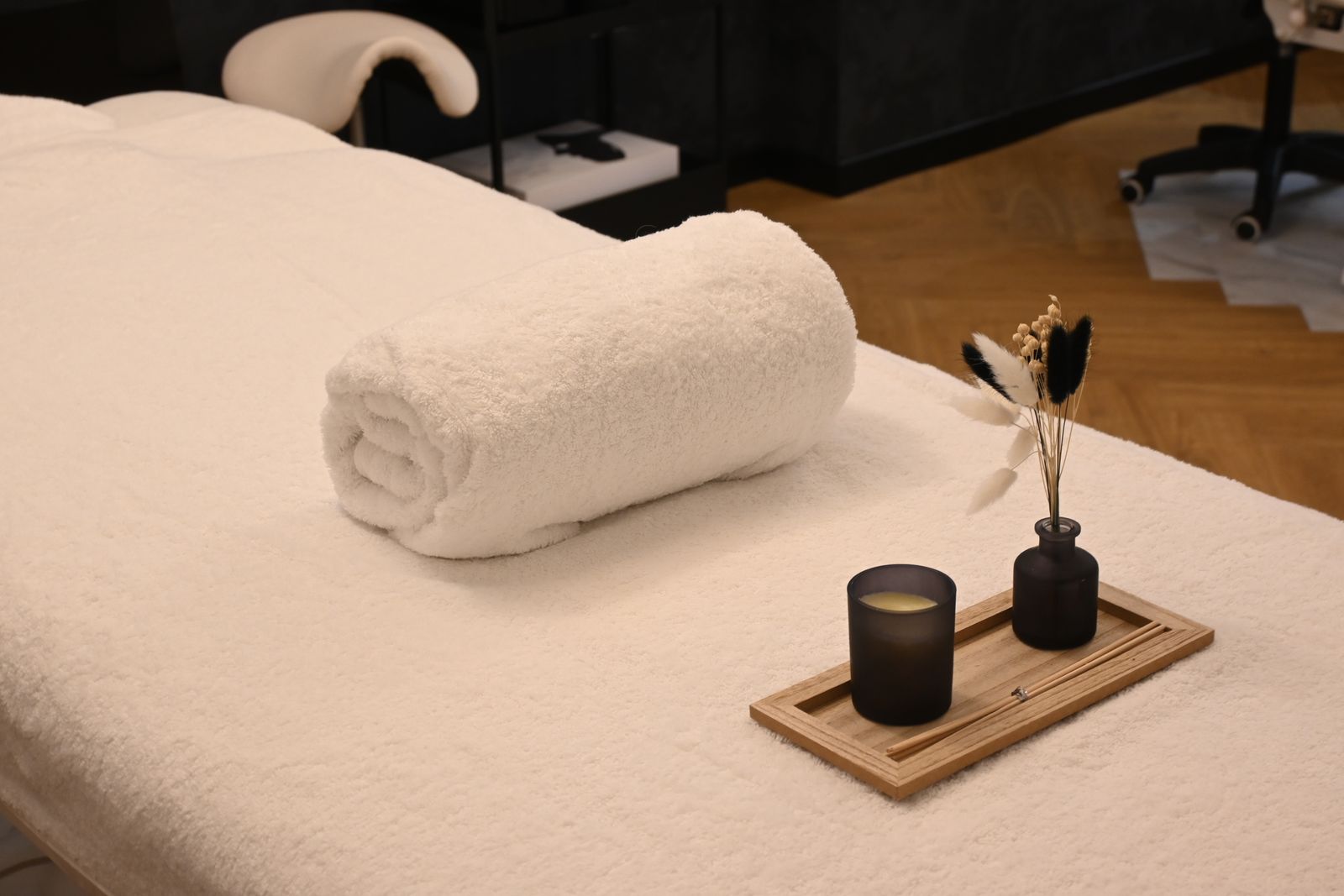 A rolled white towel on a massage table with a candle and a small vase