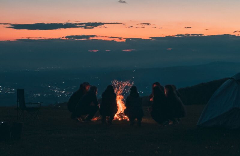 A group sitting around a campfire on a hillside at dusk