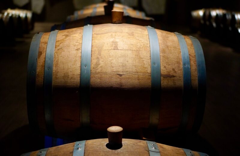 Oak wine barrels in a dark cellar, one lit by a beam of light
