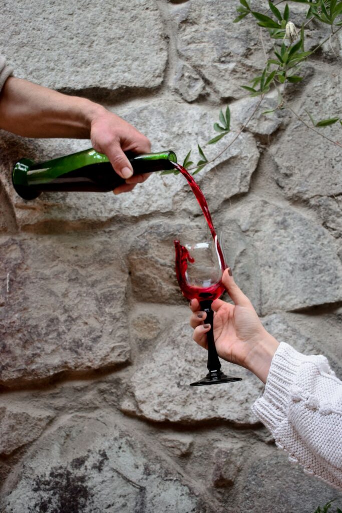 Red wine poured from a bottle into a glass held against a rough stone wall