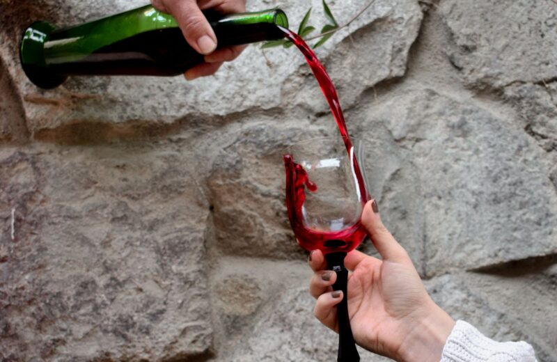 Red wine poured from a bottle into a glass held against a rough stone wall