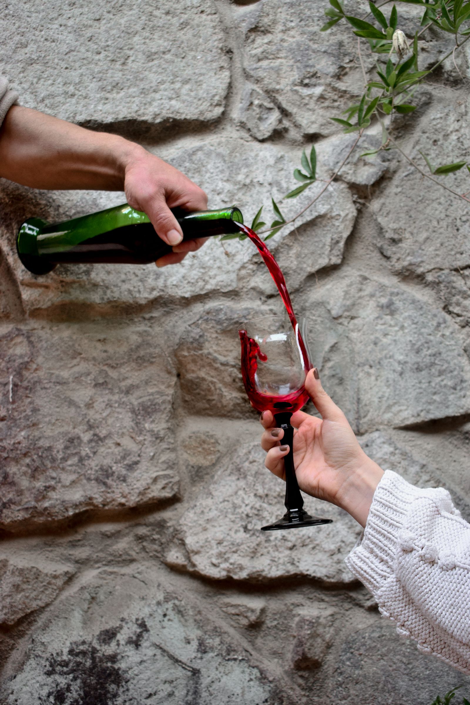 Red wine poured from a bottle into a glass held against a rough stone wall
