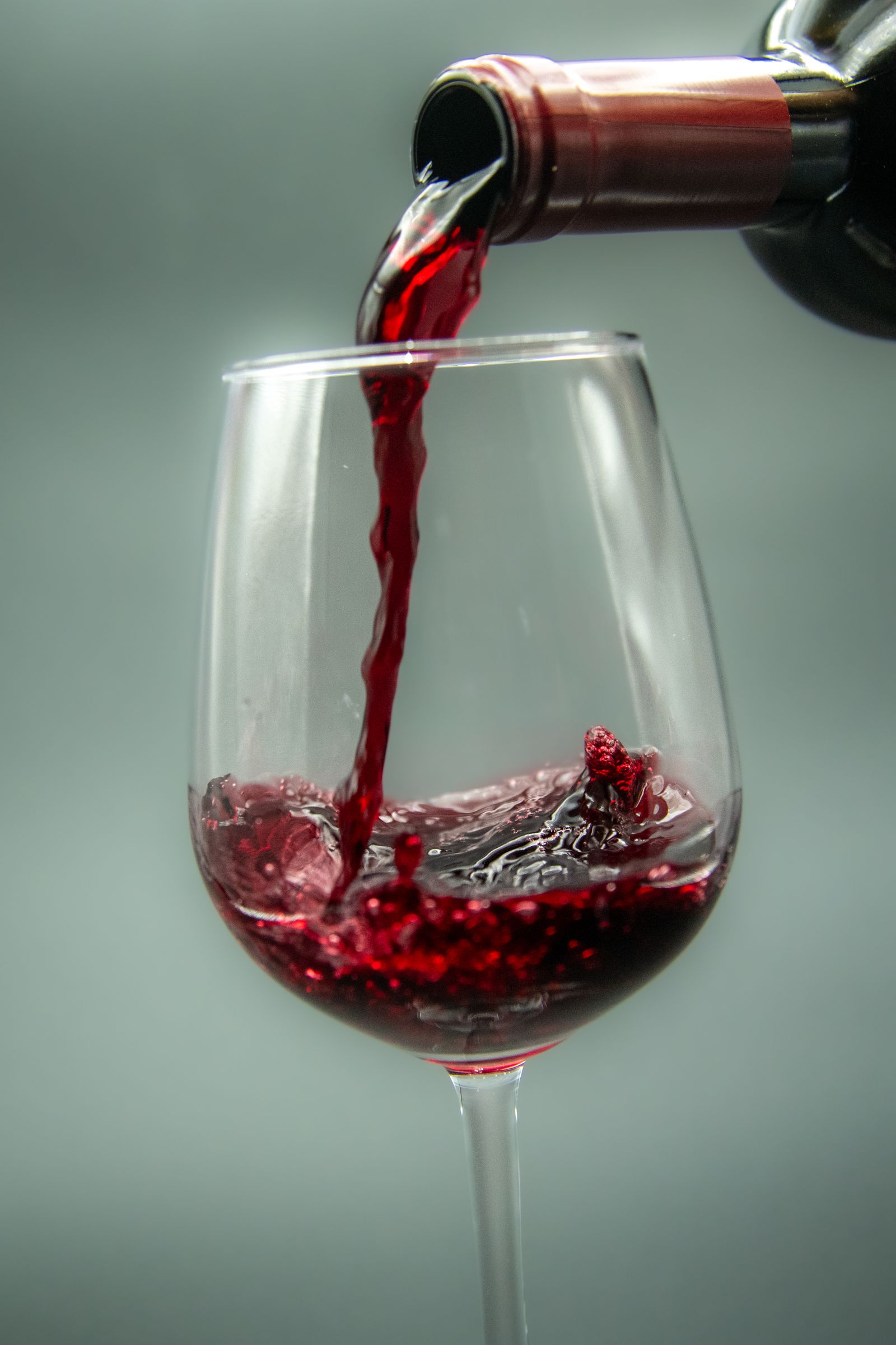 Red wine being poured into a large glass against a grey-green background