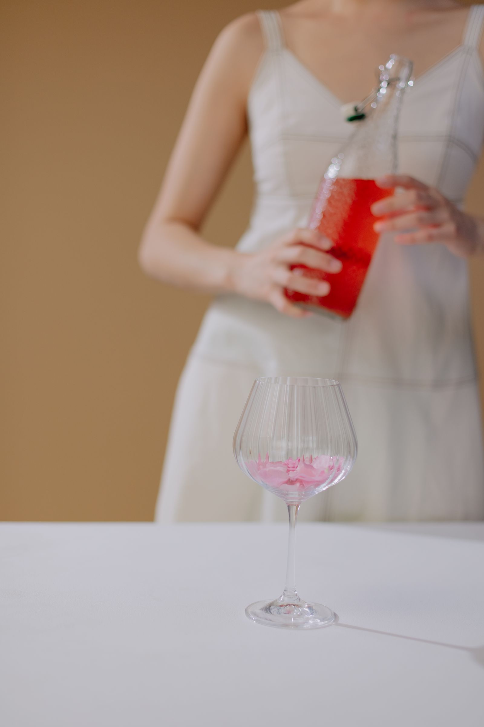 A person in white pouring pale rosé into a stemmed glass