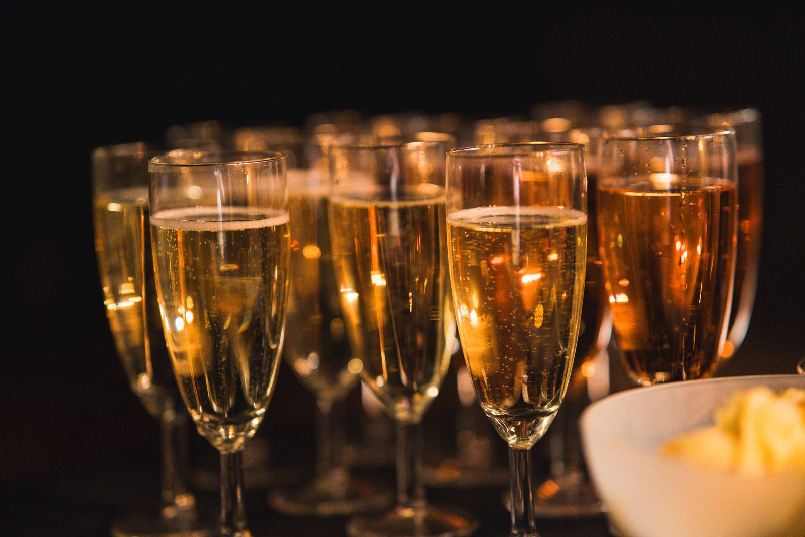 Glasses of sparkling wine lined up in low light, small lights glowing behind them