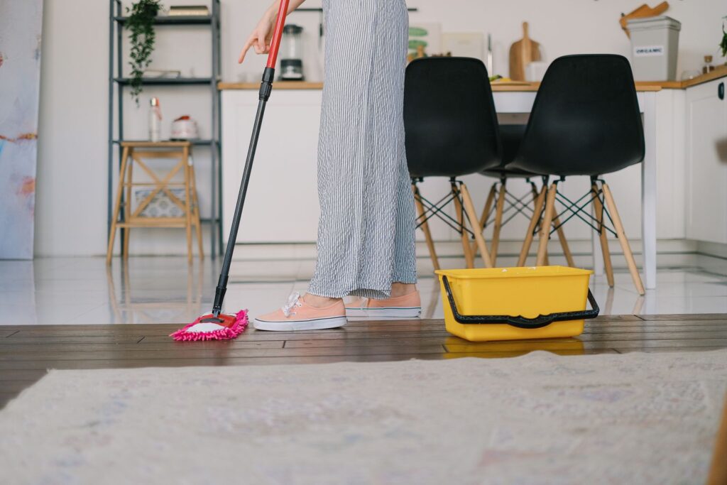 A cleaner dipping a mop into a bucket beside a wooden floor