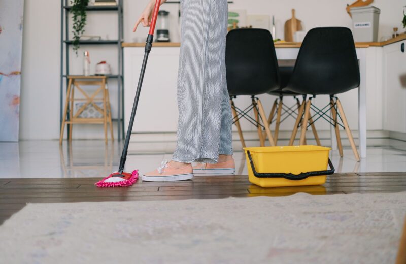 A cleaner dipping a mop into a bucket beside a wooden floor