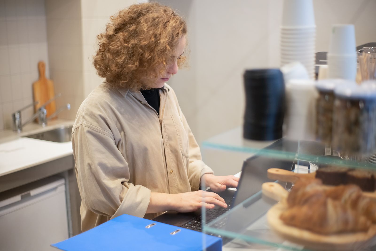 A café owner working on a laptop behind the counter, pastries in the foreground