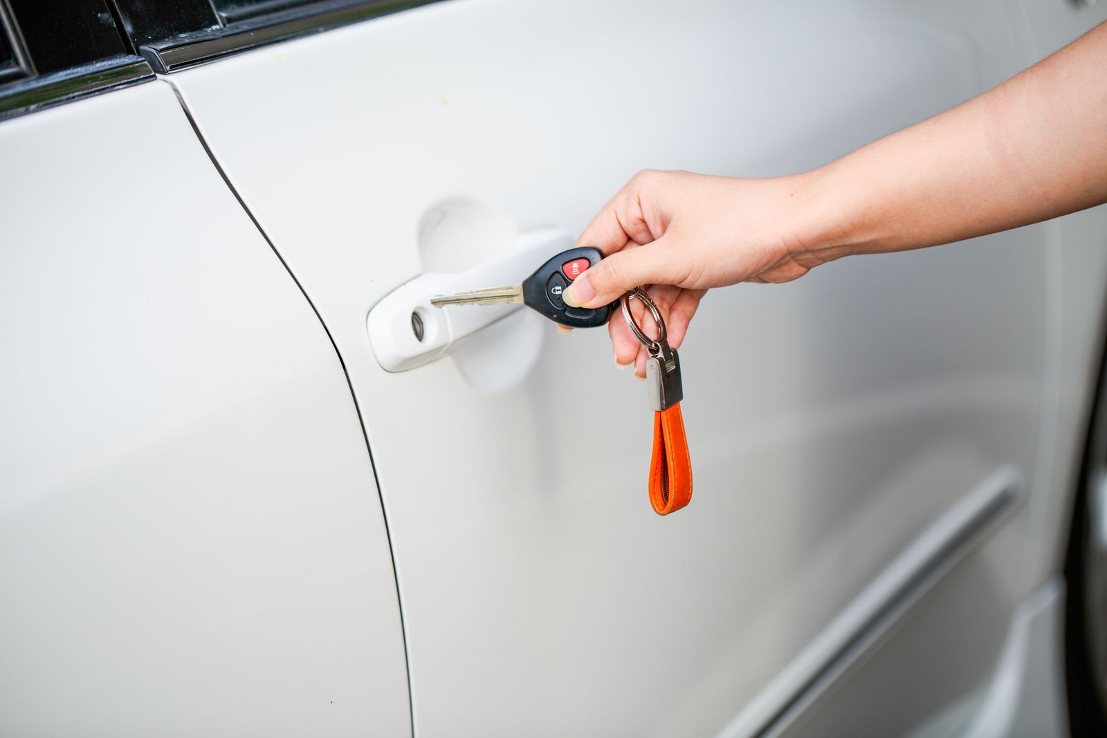 A hand unlocking the door of a white car with a key