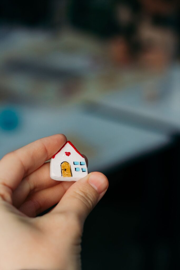 A hand holding a tiny white model house with a red roof