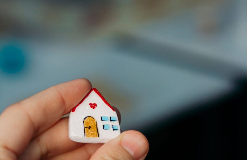 A hand holding a tiny white model house with a red roof