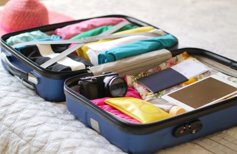 An open suitcase packed with clothes, a camera and a passport