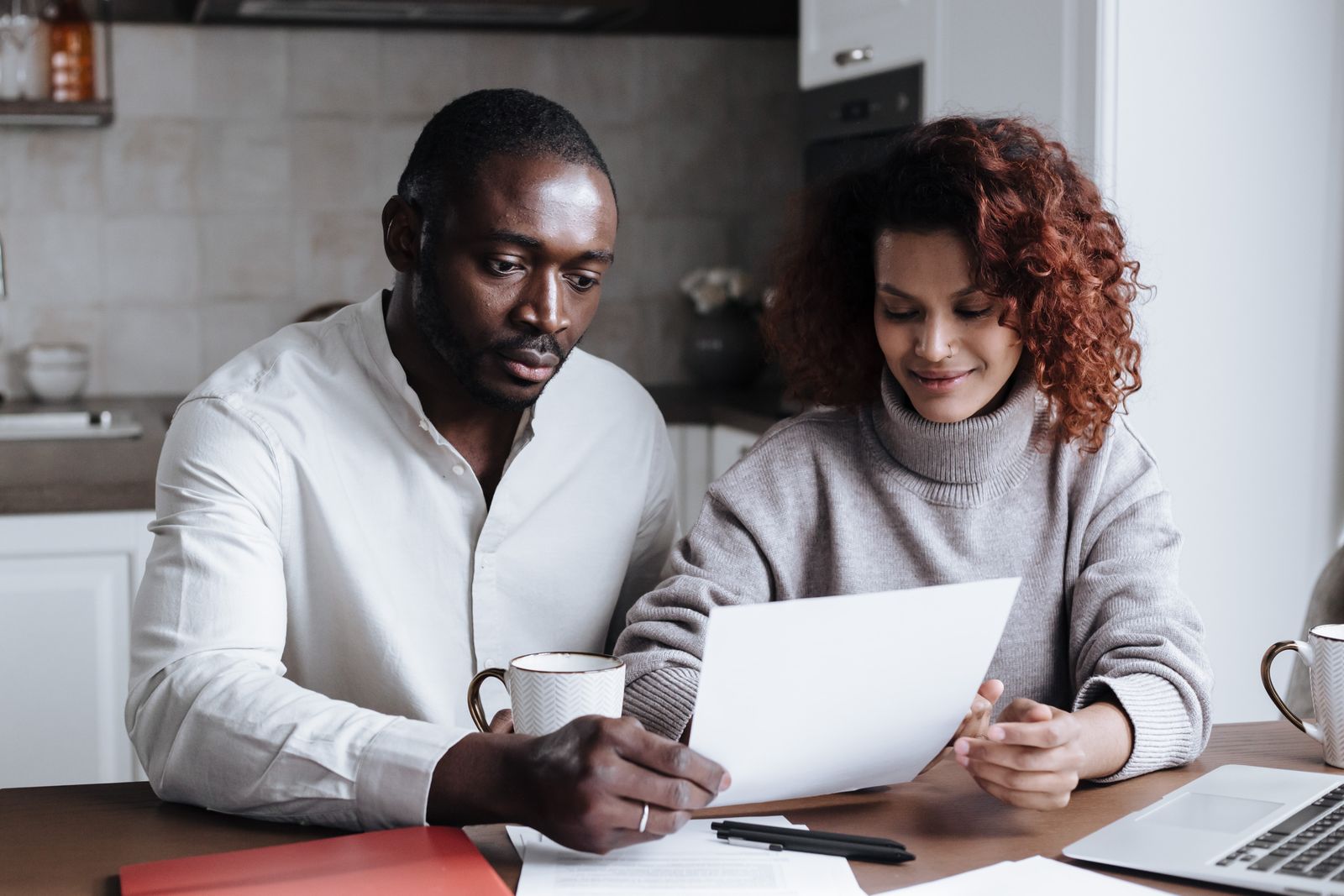 A couple going through paperwork together at a kitchen table with a laptop and coffee