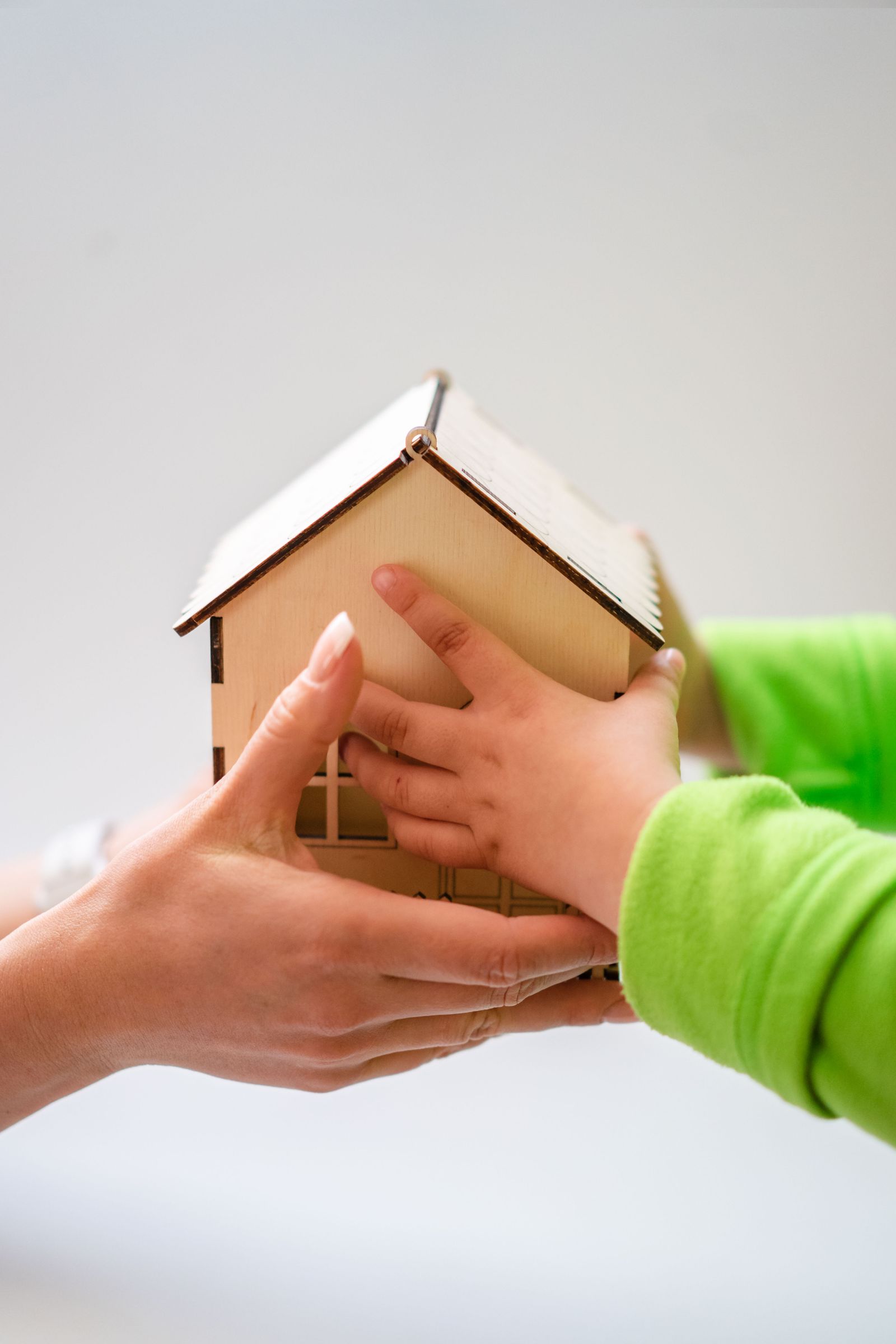 A child's hands and an adult's hands holding a small wooden model house
