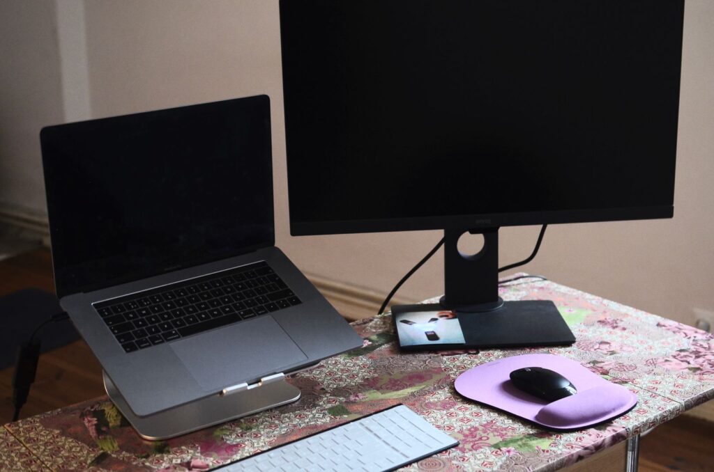 A laptop on a stand next to a monitor, keyboard and mouse on a desk
