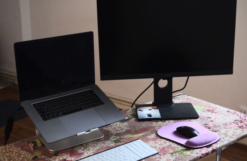 A laptop on a stand next to a monitor, keyboard and mouse on a desk