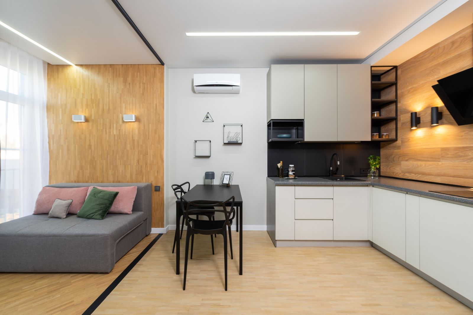 Studio flat with a sofa by the window, oak panelling and a compact kitchen behind the dining table