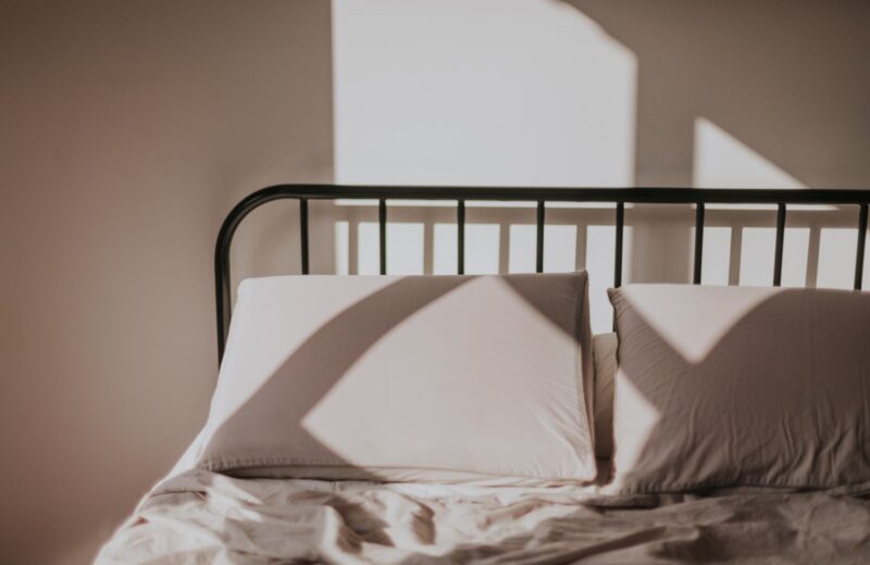 Morning sun casting window shadows across a bed with linen pillows