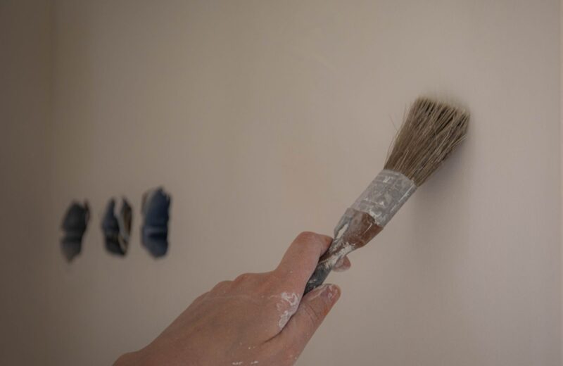 A hand painting a white wall beside three test patches of colour