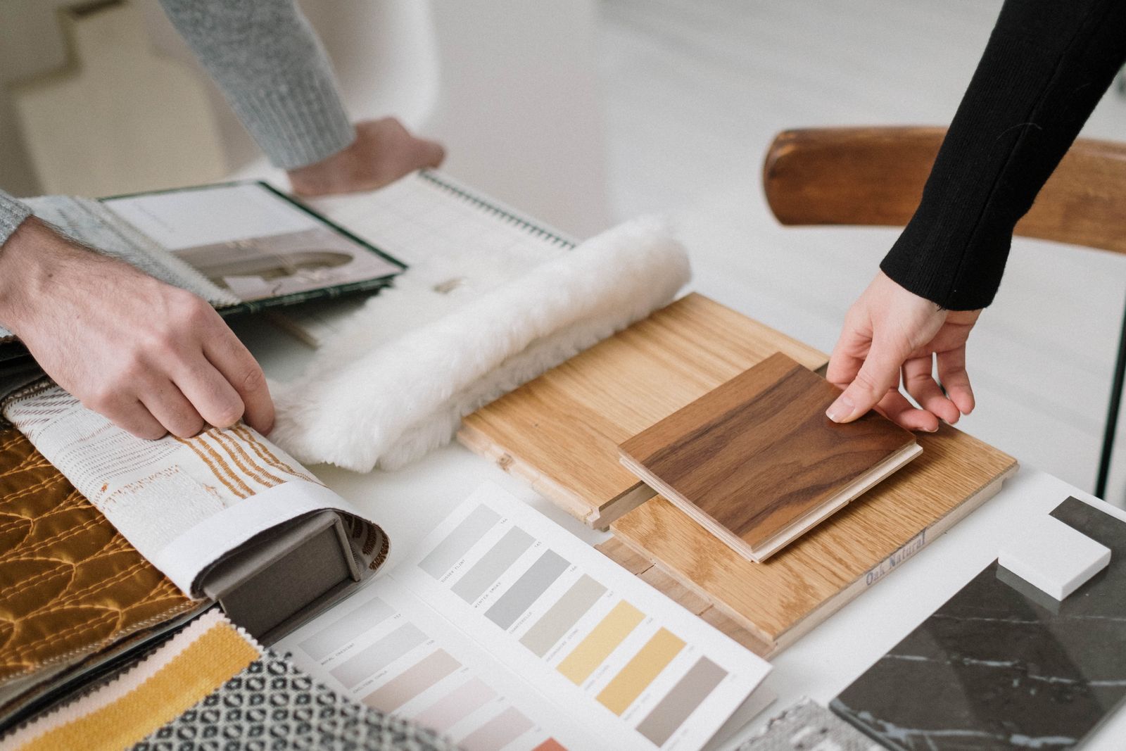 Hands comparing oak veneer, fabric and stone samples on a table