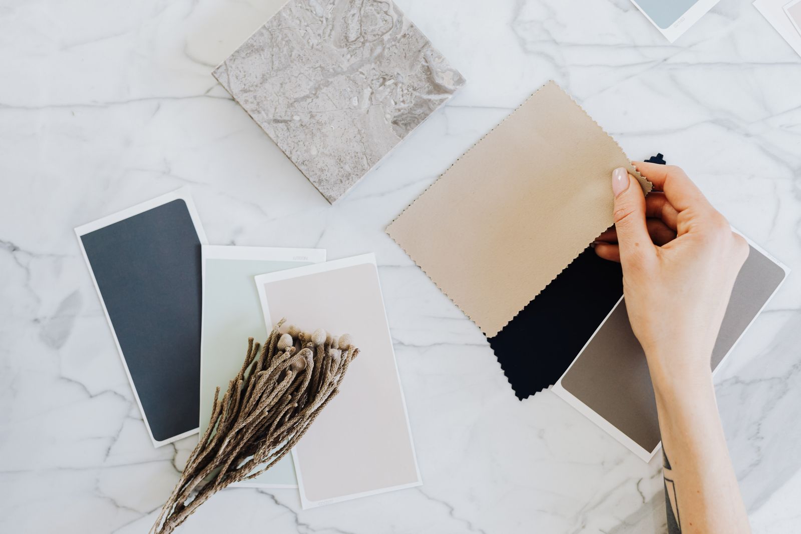Hands holding fabric and paint swatches over a marble desk