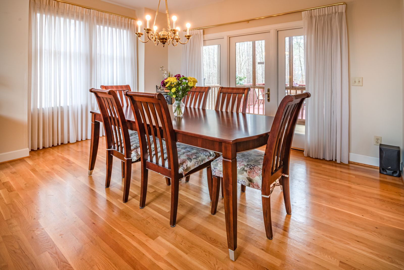 A dining room with a long wooden table, eight wooden chairs and a chandelier by the windows