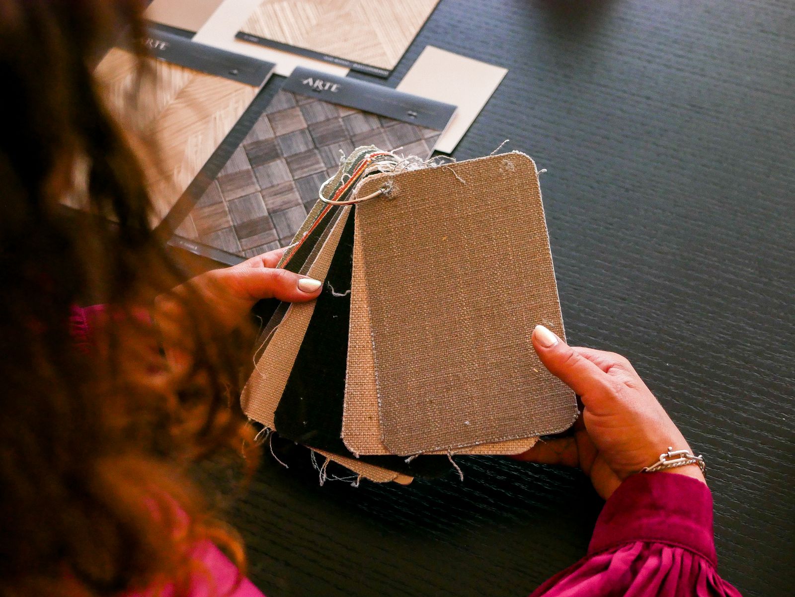 Hands holding upholstery fabric samples over a dark table