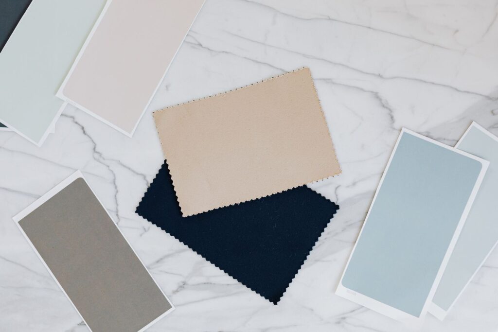 Fabric and colour samples in neutral tones and navy laid out on a white marble table