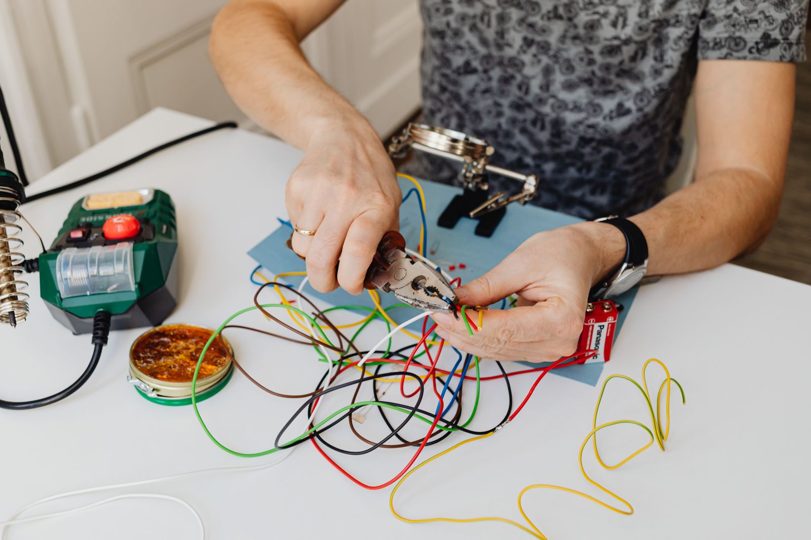 Hands stripping coloured wires at a practice bench with pliers