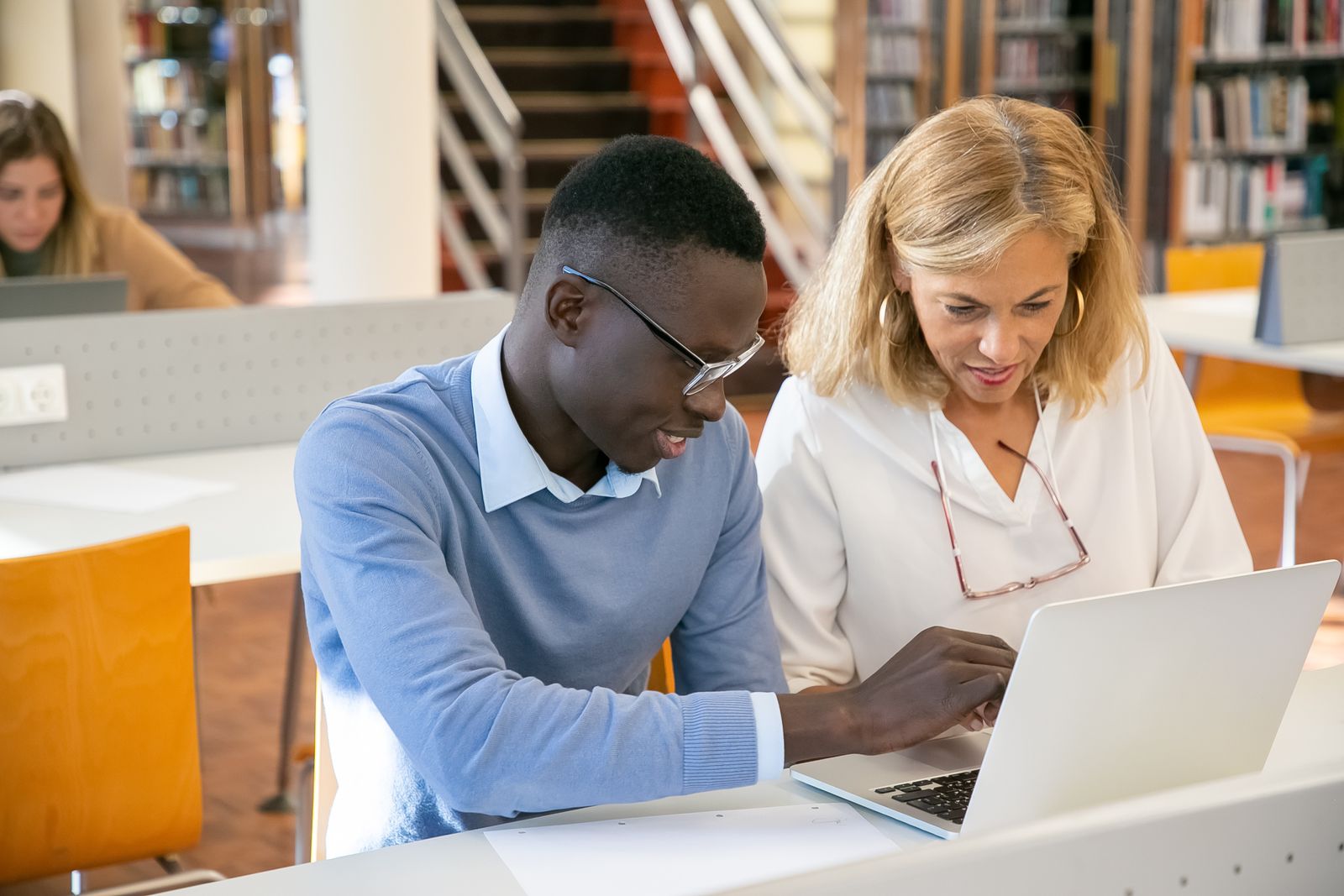 A helper and a job seeker working through an application on a laptop in a library